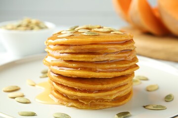 Tasty pumpkin pancakes with seeds on table, closeup