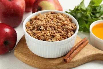 Delicious apple crisp in bowl, fresh fruits, cinnamon stick, honey and mint on white table, closeup