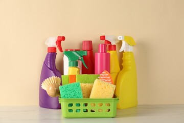 Different cleaning products and supplies on white marble table against beige background