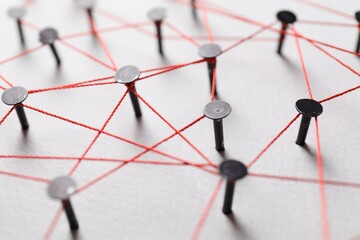 Network connection. Nails linked together by thread on white table, closeup
