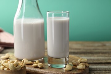 Fresh cashew milk in glass, bottle and nuts on wooden table against green background, closeup