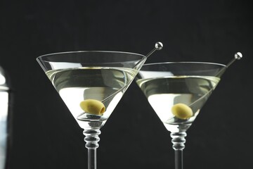 Martini cocktail with olives in glasses on black background, closeup