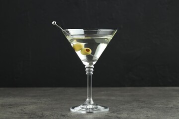 Martini cocktail with olives in glass on grey table against black background