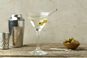 Martini cocktail with olives in glass and shaker on wooden table
