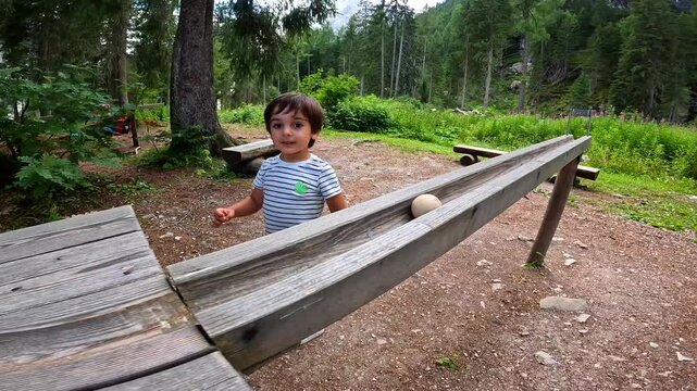 Child playing with wooden marble run in a forest near lake braies, dolomites, italy