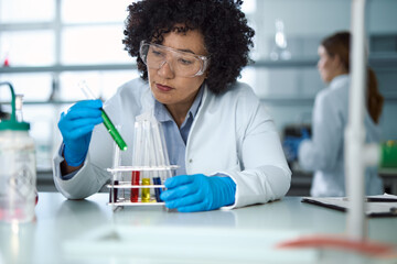 Multiracial female chemist examining chemicals for her scientific experiment in laboratory.