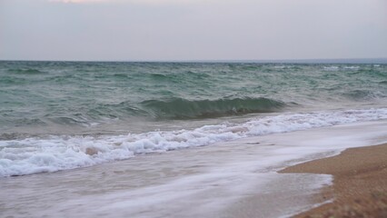 Waves crashing on the sand at a beach with the ocean behind