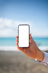 Man holds phone in hand against blurry sea background, blank space on screen