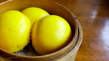 Three golden-yellow baozi chinese steamed buns arranged in a bamboo steamer basket, placed on a wooden table, exuding a warm and appetizing appearance