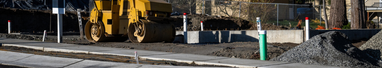 Yellow steam roller on a new home construction job site with new sidewalk and asphalt street, heavy equipment parked on a quiet sunny day
