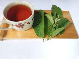 Boiled water or guava leaf tea (Psidium guajava), contains antioxidants and is useful for treating diarrhea on the wooden mat isolated on white background, copy space