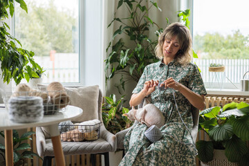 A young beautiful smiling girl crochets from gray yarn and strokes a sphinx cat.