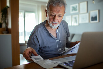 Senior man managing bills and paperwork at home with laptop