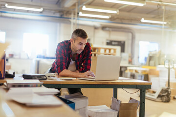 Man working on laptop in printing warehouse