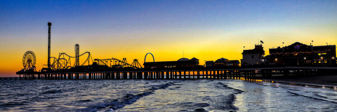 Fototapeta Galveston, Texas - 11-23-2024. A panorama of an amusement park on a large pier stretching out into the Gulf of Mexico at sunset.