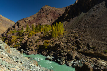 Clear green water of Zanskar river flowing through barren mountains with rocks in Ladakh.