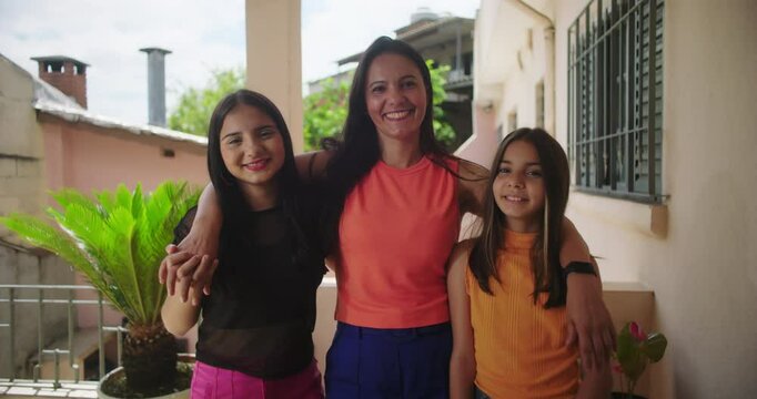 Mother with two daughters posing together on sunny porch, smiling warmly, showcasing family bond, connection, and love in relaxed outdoor setting