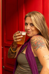 Woman with tattoos enjoying a beer in a vibrant red background