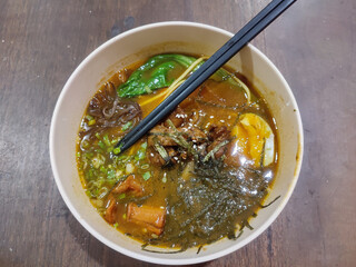 A bowl of flavorful ramen with rich brown broth, topped with seaweed, egg, vegetables, and sliced meat. Perfect for Asian food themes and culinary designs.