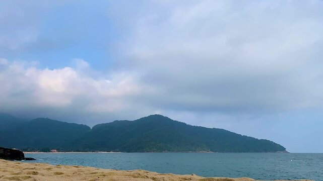 Time-lapse da baia com nuvens na montanha em dia parcialmente nublado e com mar&eacute; bem baixa. Ao fundo, algumas embarca&ccedil;&otilde;es navegando e uma montanha com floresta de Mata Atl&acirc;ntica envolvida pela neblina