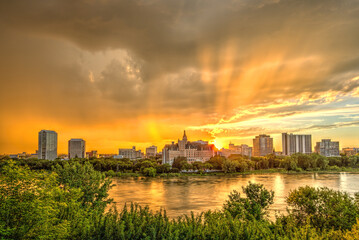 A city skyline is reflected in the water, with the sun setting in the background