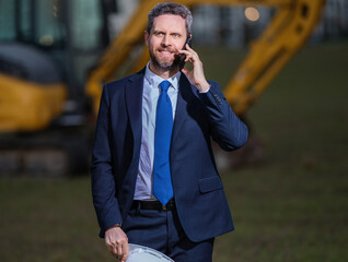 Buider man in suit and hardhat. Construction investor. Business man investor in front of construction site. Successful investor. Handsome man in suit and hardhat at building construction.