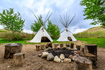 Obraz premium Two teepees are set up in a grassy field with a fire pit in the center