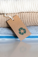 Knitted warm clothes neatly folded heap with craft tag recycling material circle arrow closeup