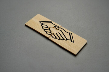Two puzzle pieces with a handshake symbol, representing partnership, cooperation, and agreement.