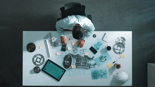 Top down view of skilled engineer writing and planning turbine engine design while sitting at meeting table with gear and electronic generator scatter around. Technician taking a note. Alimentation.