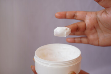 Indian young women use fingers to take out moisturizer cream from the jar. Skin care, body moisturizing lotion, routine in the morning, health and beauty care concept. Selective focus on finger tip.