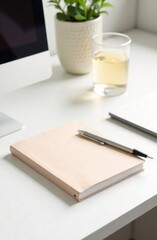 A minimalist workspace features a notebook and pen on a desk alongside a glass of refreshing water and a plant