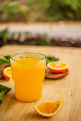 A glass of freshly squeezed orange juice on a wooden table surrounded by orange slices and orange leaves