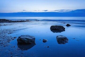 Fototapeta premium Serene coastal landscape at dusk with stones and calm water reflections.