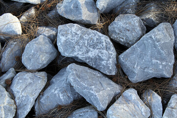 Pile of grey gray rocks sitting on fallen pine needles abstract textured background