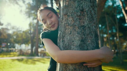 Young woman hugs a tree in a park, smiling and enjoying the moment. Surrounded by nature, she radiates happiness and tranquility, embracing the beauty of her environment