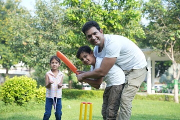happy indian father and son play cricket sport in summer park. Family play game outdoor having fun. together. Picnic. 