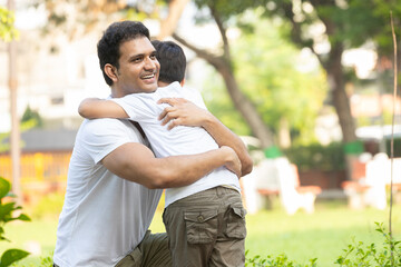 happy indian father hugging or embracing his son in park. parenting concept.