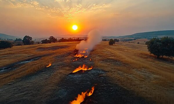 Sunset over a field with patches of fire and smoke.