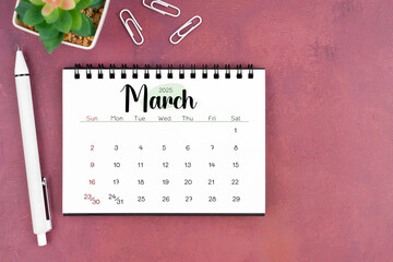 March desk calendar for 2025 year and pen on old red cover. Flat lay.