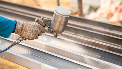 Construction worker painting metal structure surface coating with a spray gun at construction site....