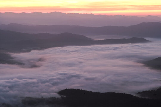 Panorama view layers of mountain with the fluffy white fog between the mountains and orange sunrise sky in background