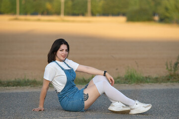 Portrait of a young beautiful dark-haired girl in a denim sundress outdoors.