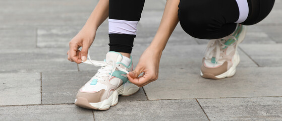 Naklejka premium Young woman in sportswear and stylish sneakers tying shoe laces outdoors, closeup