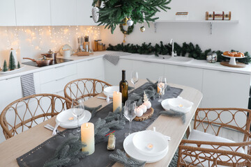 Interior of modern kitchen with festive table setting, glowing lights and Christmas decorations