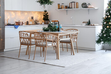 Interior of modern kitchen with festive table setting, glowing lights and Christmas decorations