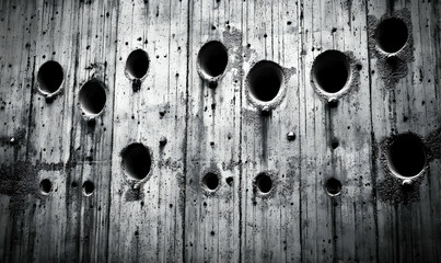 Abstract black and white image of a concrete wall with numerous circular holes, showcasing texture and pattern.