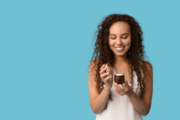 Beautiful young African-American woman with jar of face cream on blue background