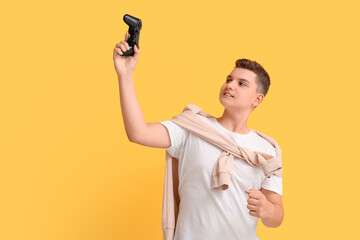 Teenage boy with game pad celebrating success on yellow background