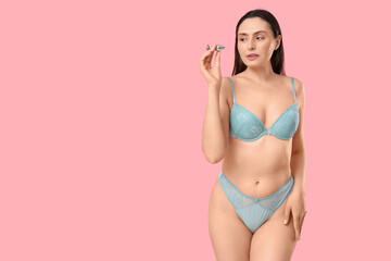 Beautiful young woman in underwear with anal plug from sex shop on pink background